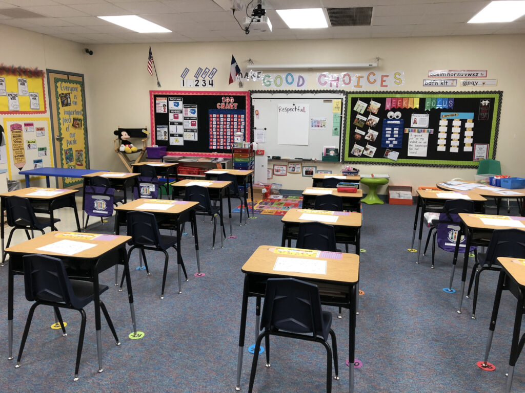 An elementary classroom is decorated with visuals and has numerous desks spaced out.