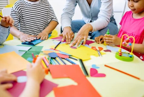 Image of a teaacher and studnets sitting at a table with craft supplies