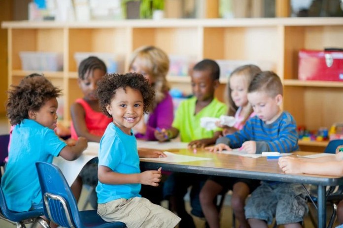 A group of young children sits at a table in a classroom