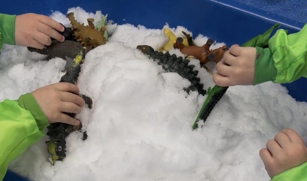 Students playing with dinosaur toys in a bin filled with snow