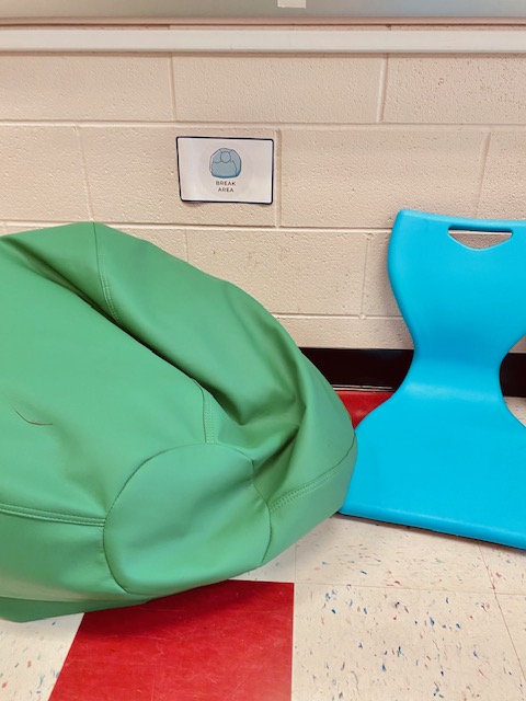 A green beanbag and blue chair on the floor of a classroom, with a label on the wall that says "break area"