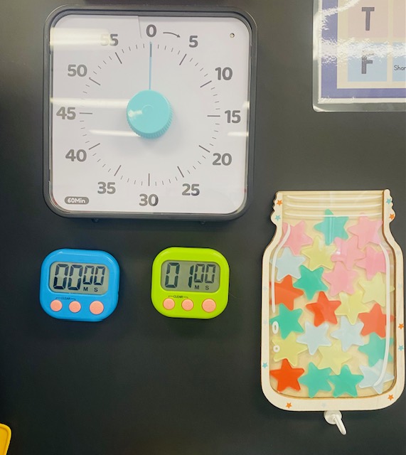 Visual timers on a chalkboard - a large analog clock-style timer and two smaller personal digital timers.