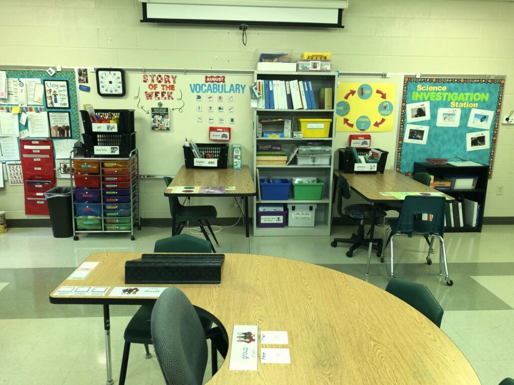Classroom side view of part of a u shaped group table and 2 other rectangular tables for grouping students working in different centers.