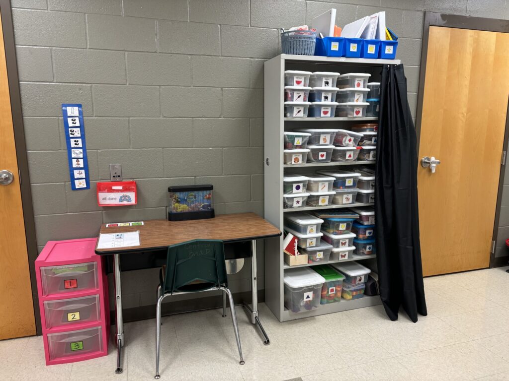 An independent desk sits next to a task box shelf, along with a 3 drawer work system. A task analysis for routine is on the wall.