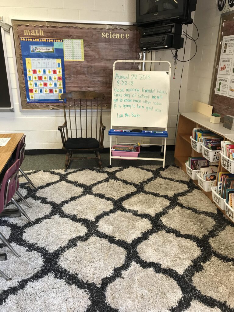 Image showing a rocking chair on a carpet next to a white board greeting students for the first day of school