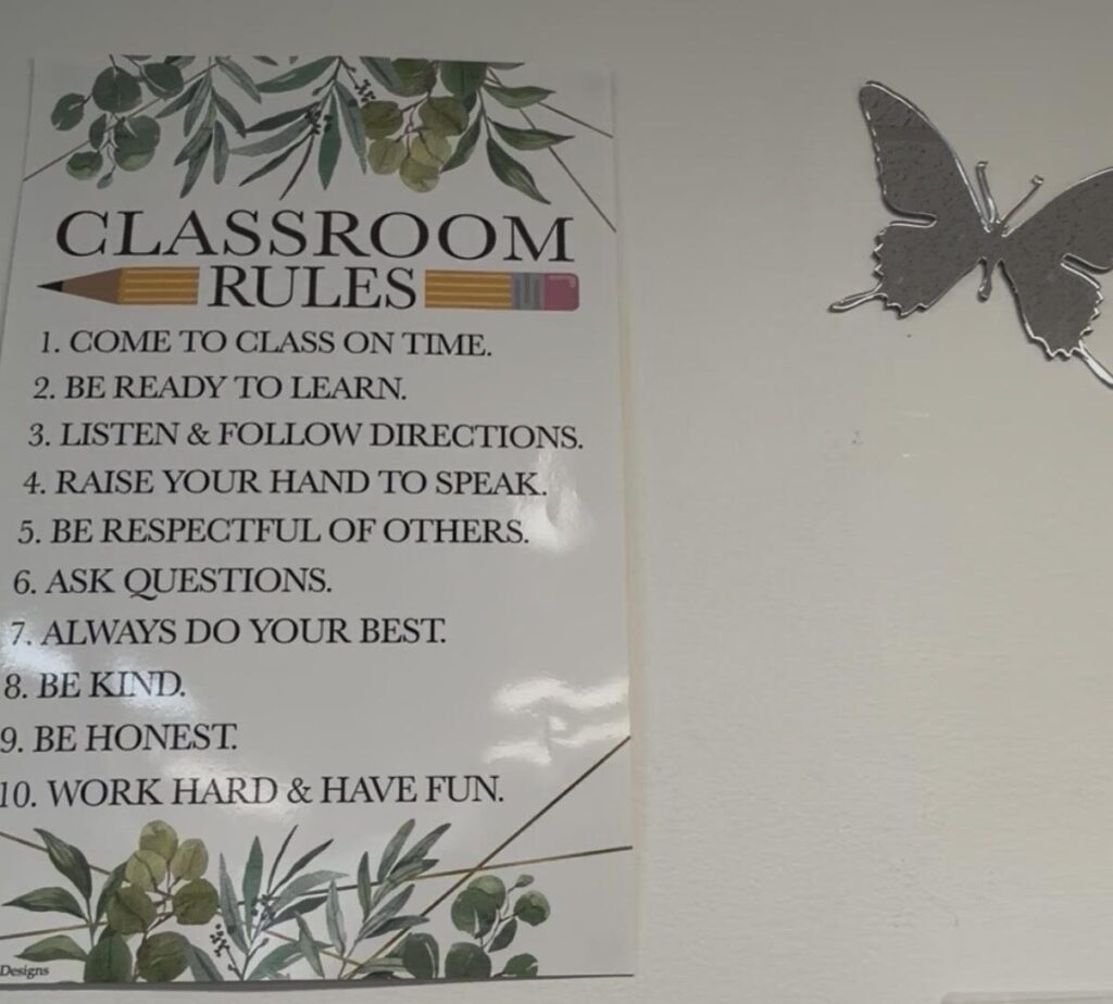 Classroom rules poster on a whiteboard next to a silver butterfly decoration