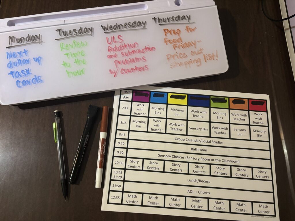 A table top whiteboard shows an outline of the week's math center plans along side a daily schedule with times and descriptions of activities