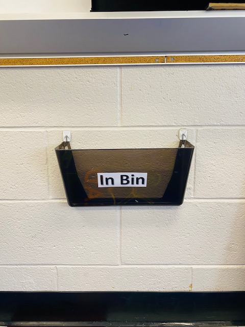 A black bin on a classroom wall labeled "in bin"