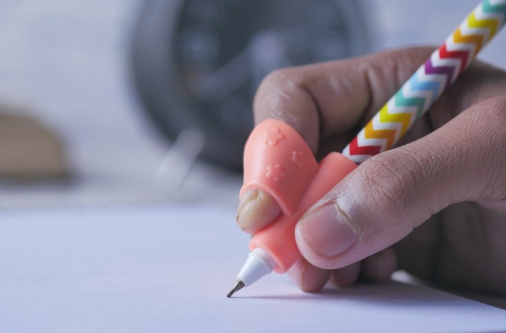 a child holds a colorful pencil with a finger grip