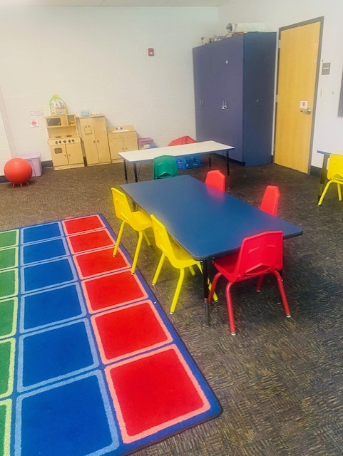 a view of a classroom with a colorful rug, and student table with colorful charis