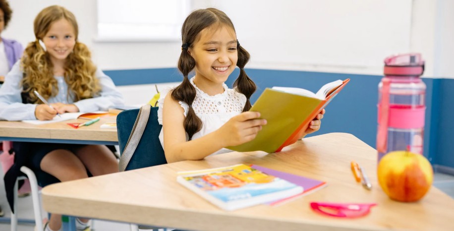 A girl reads a book at a desk in a classroom