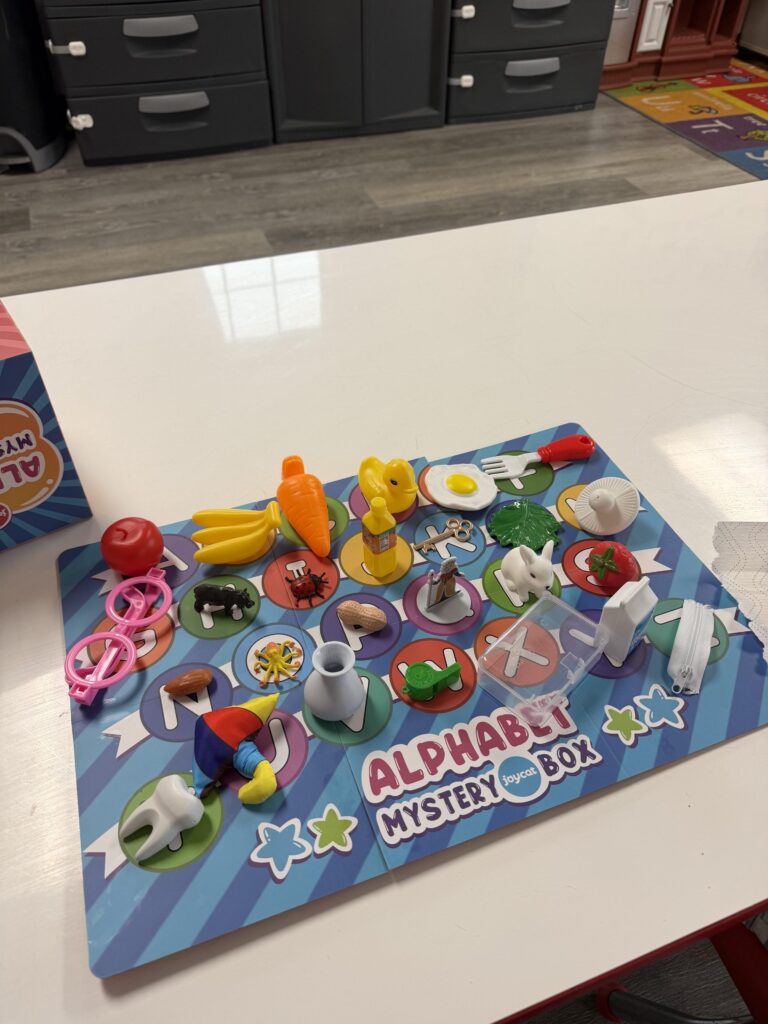 Image of an "alphabet mystery box" game with 26 objects placed on all the letters of the alphabet on a board