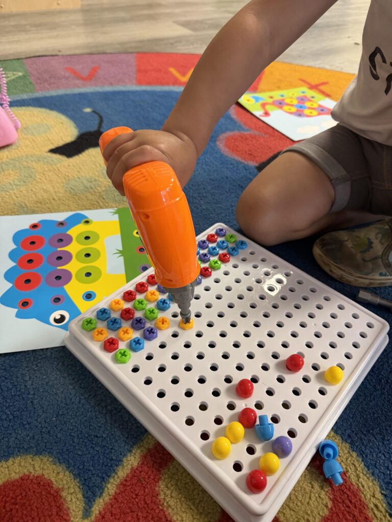 Image of a child playing with a toy drill and toy screws on a peg board