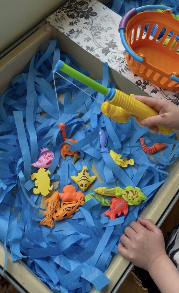Child "going fishing" with a toy fishing pole in an ocean sensory bin