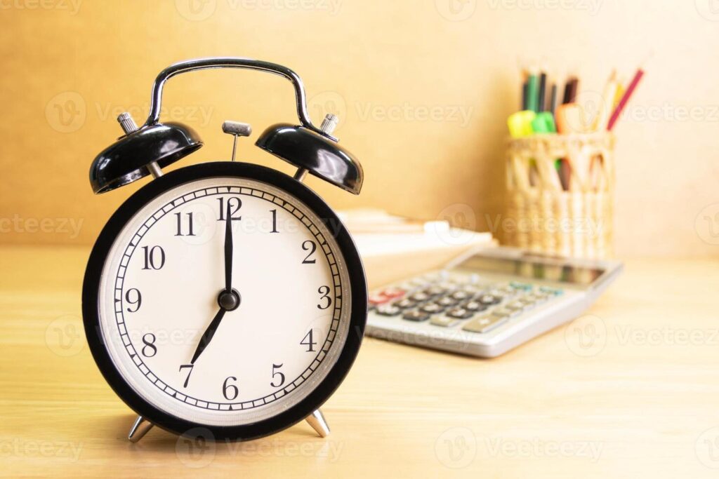 Alarm clock on a desk showing 7:00 next to a calculator and pencil holder