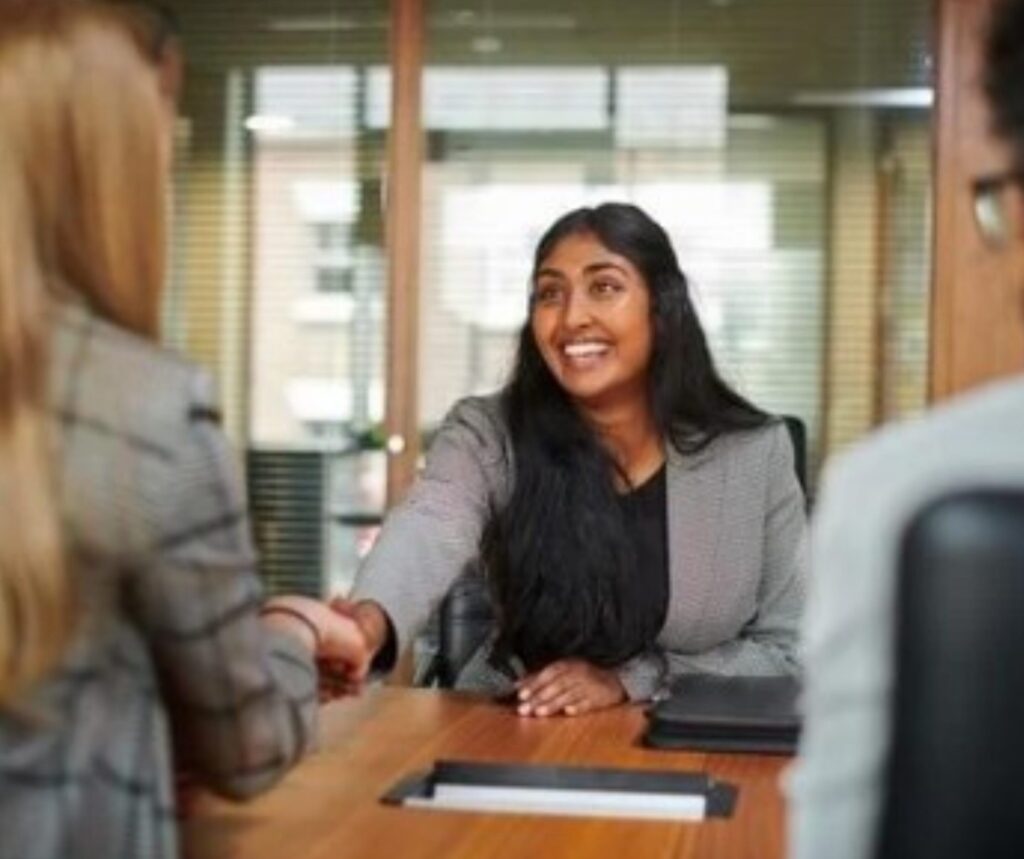 Woman sitting at a desk shaking another woman's hand