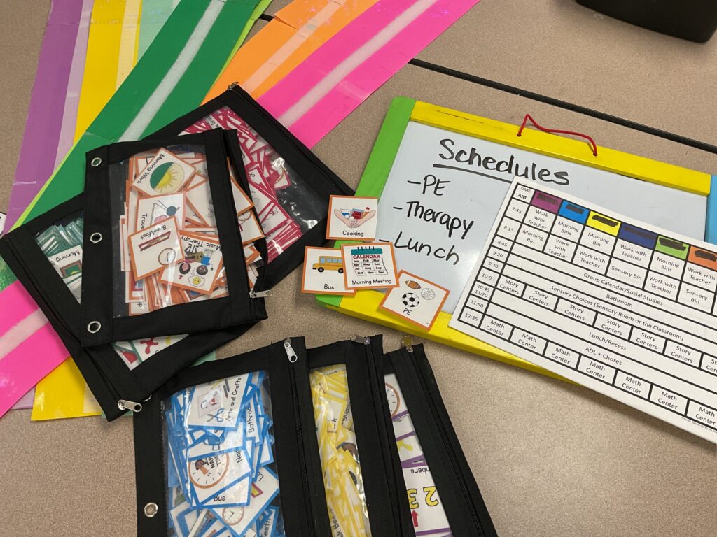 Color coded visual schedule pieces lay on a table, ready to assemble. A teacher planning schedule sheet and whiteboard are also nearby.