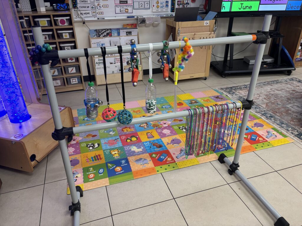 A sensory bar hangs beads, water bottles, jingle bells, and balls.