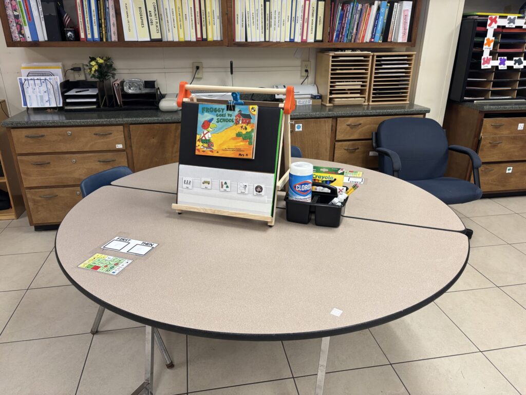 An easel holds a book paired with adapted pieces, shown on a table next to writing utensils.