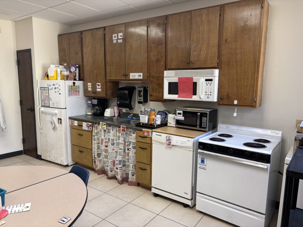 Classroom kitchen contains cabinets and shelves, as well as a refrigerator, a sink, microwave, dishwasher, and stove.