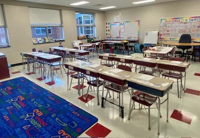 Elementary school classroom with rows of desks and a colorful carpet